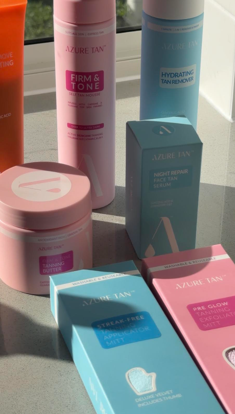 A collection of Azure Tan skincare products displayed on a countertop, including tanning mousse, serum, and a tanning butter, with bright natural light illuminating the scene.