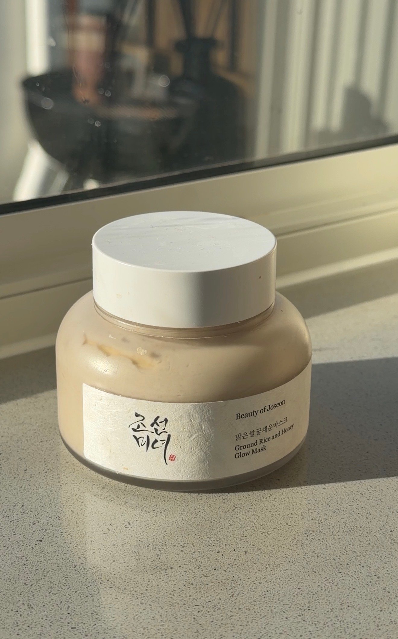 A jar of Beauty of Joseon Glow Mask sits on a windowsill, illuminated by natural light.