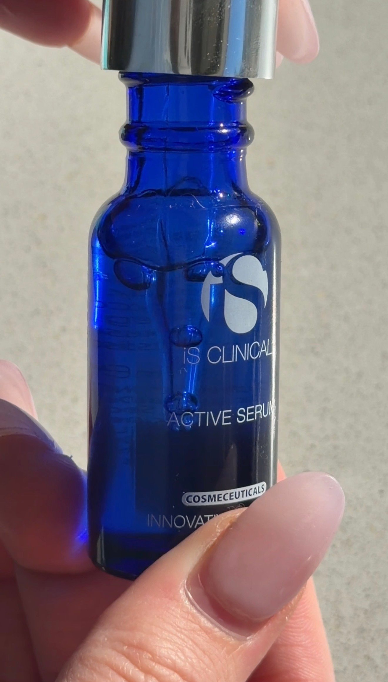 A hand holding a small blue glass bottle of IS Clinical Active Serum with a silver cap, showcasing the product label.