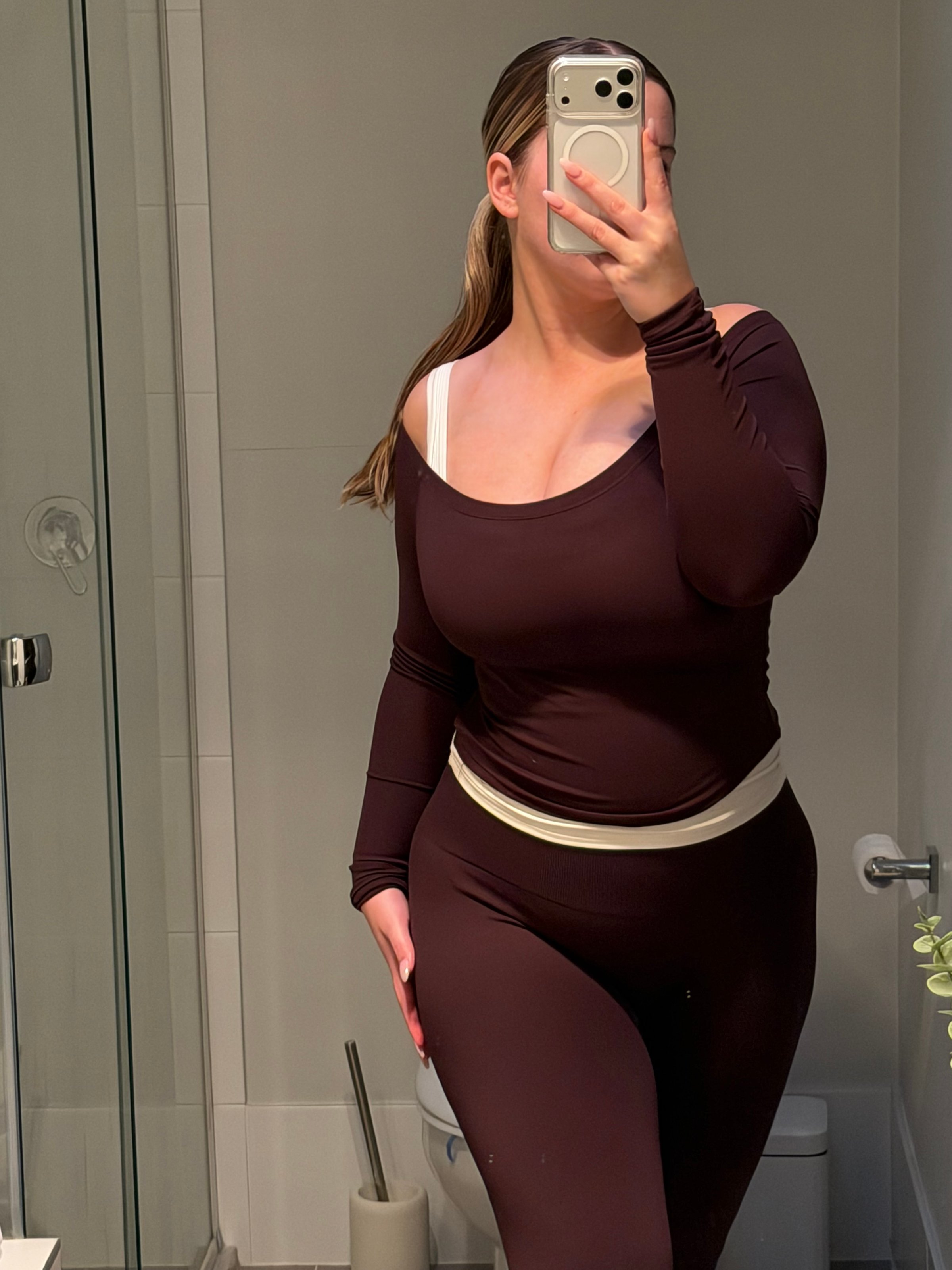 A person poses in a bathroom wearing a fitted brown outfit, showcasing a relaxed yet stylish look.