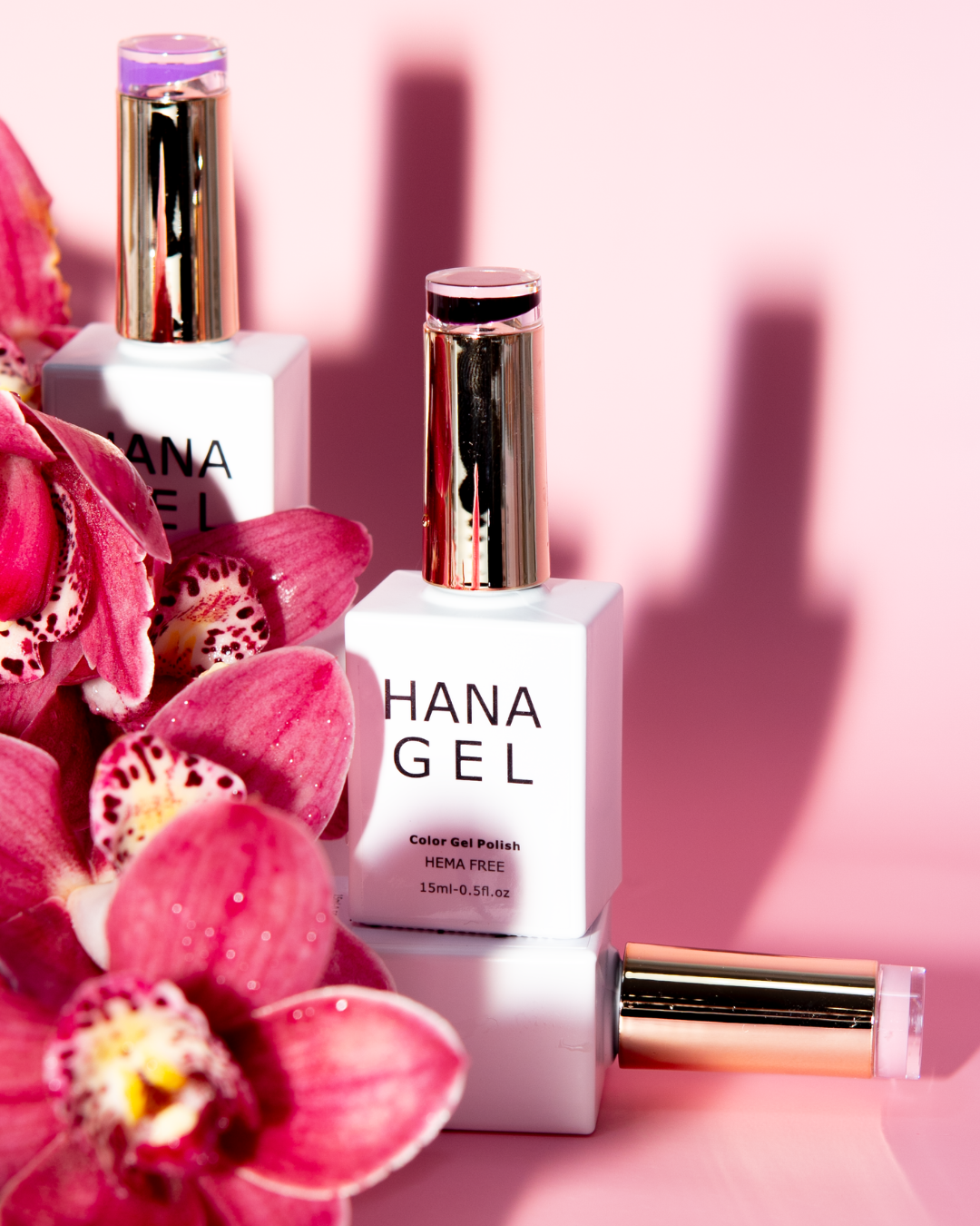 A close-up of HANA GEL nail polish bottles surrounded by vibrant pink orchids on a soft pink background.