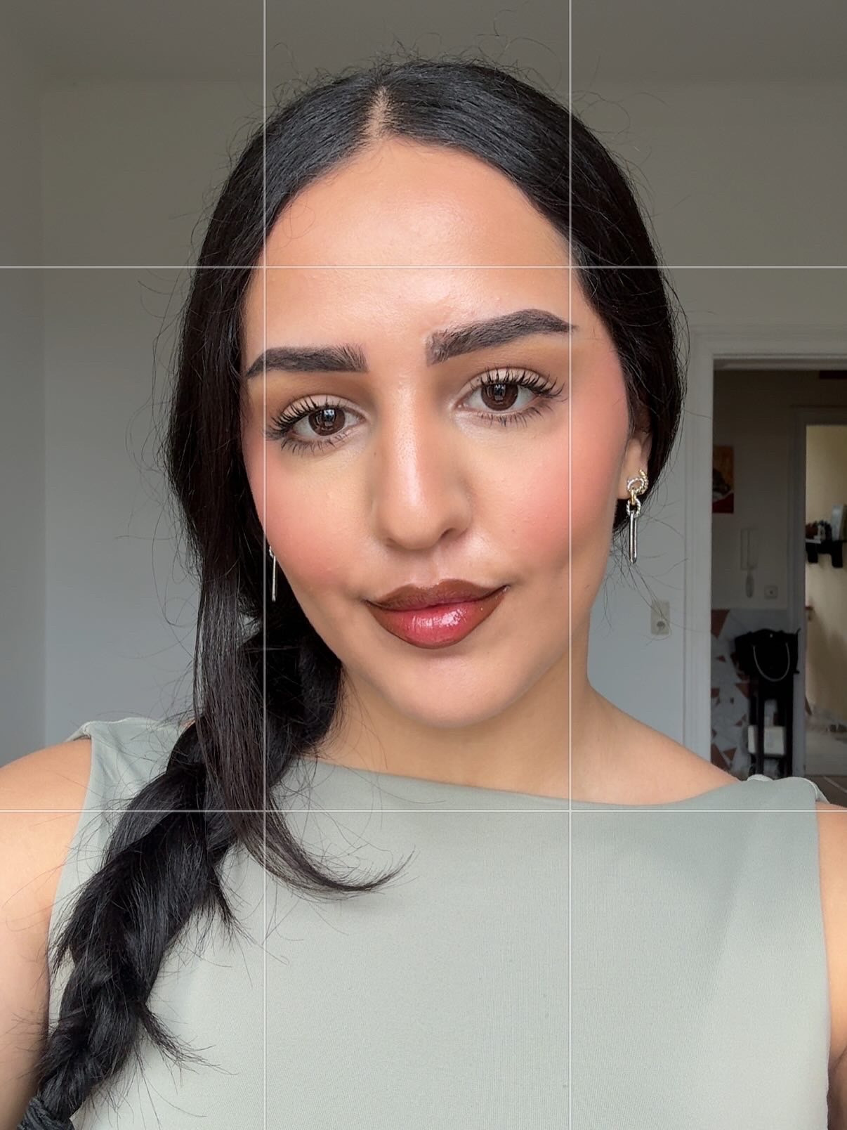 A woman with long dark hair styled in a braid, wearing a light green top and subtle makeup, poses for a close-up portrait against a neutral background.