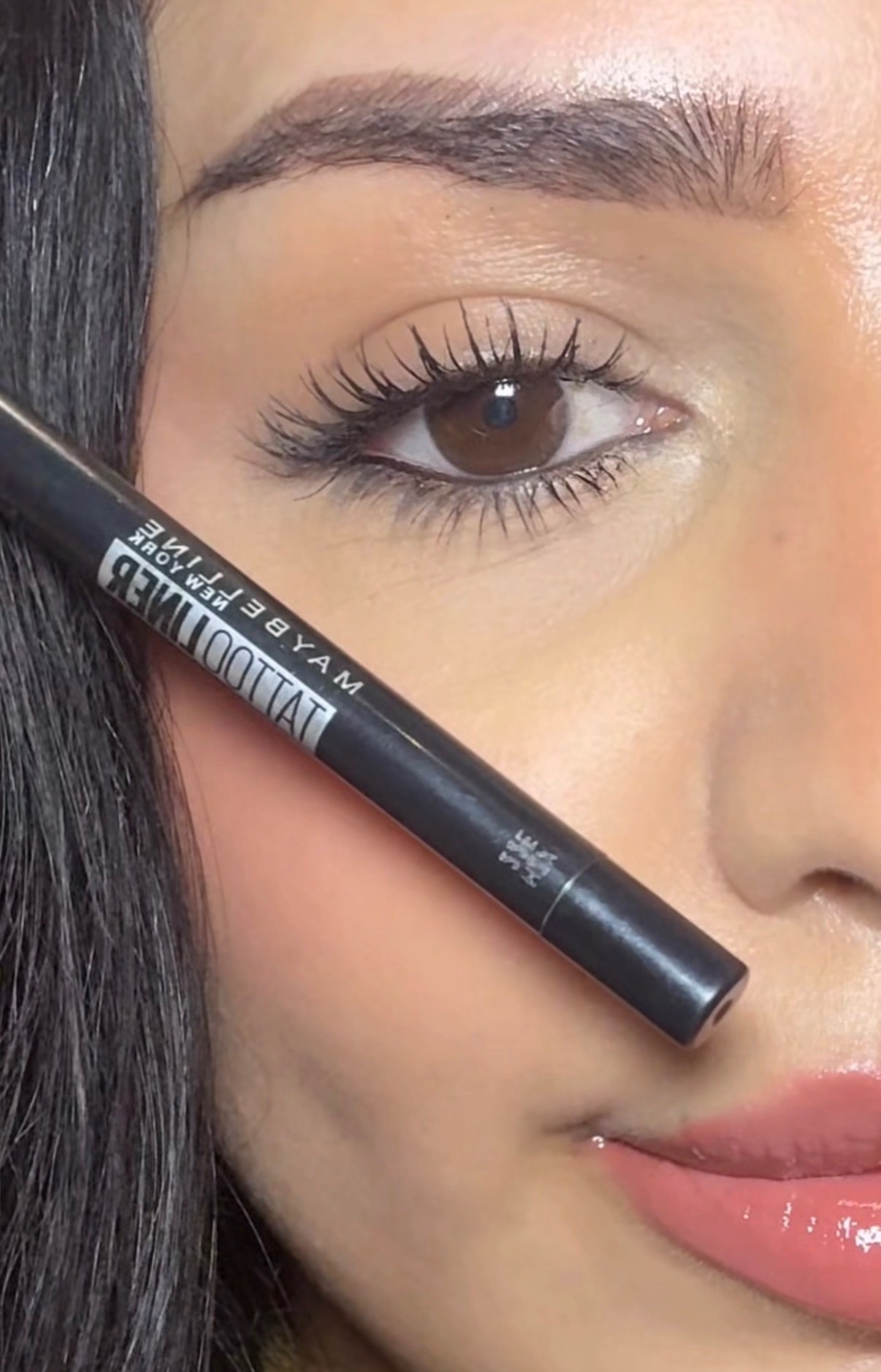Close-up of a woman's face showcasing her eye makeup, holding a black eyeliner pencil near her eye.