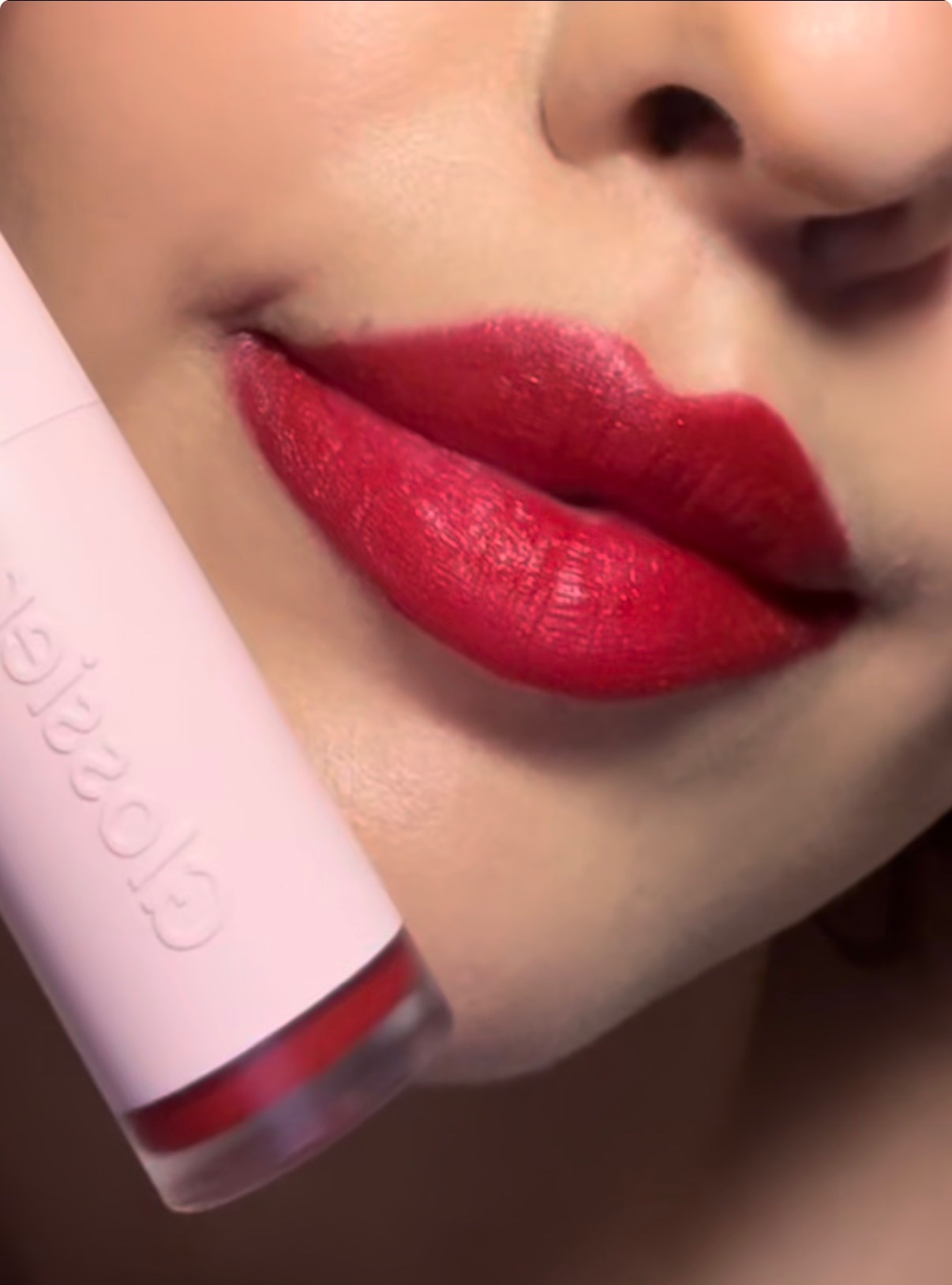 Close-up of a woman's lips adorned with vibrant red lipstick, holding a pink lipstick tube.