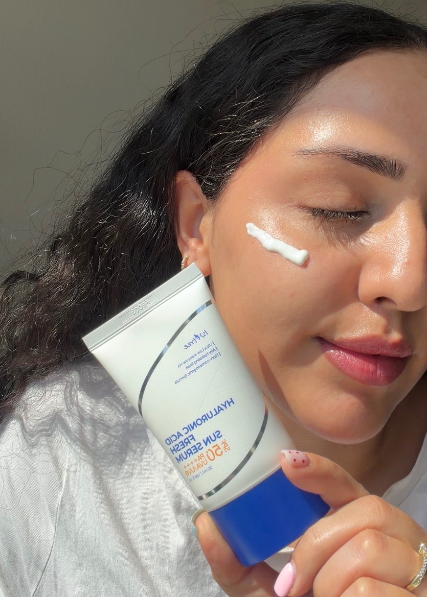 A person applying sunscreen to their face while holding a tube of Hyaluronic Acid Sun Serum.
