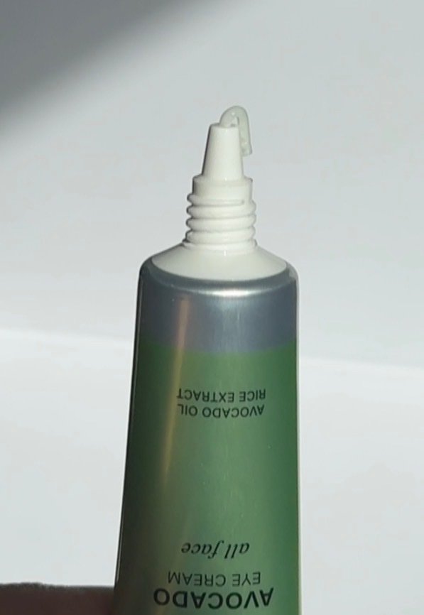 A close-up of an avocado oil eye cream tube with a green label, showcasing the nozzle at the top.