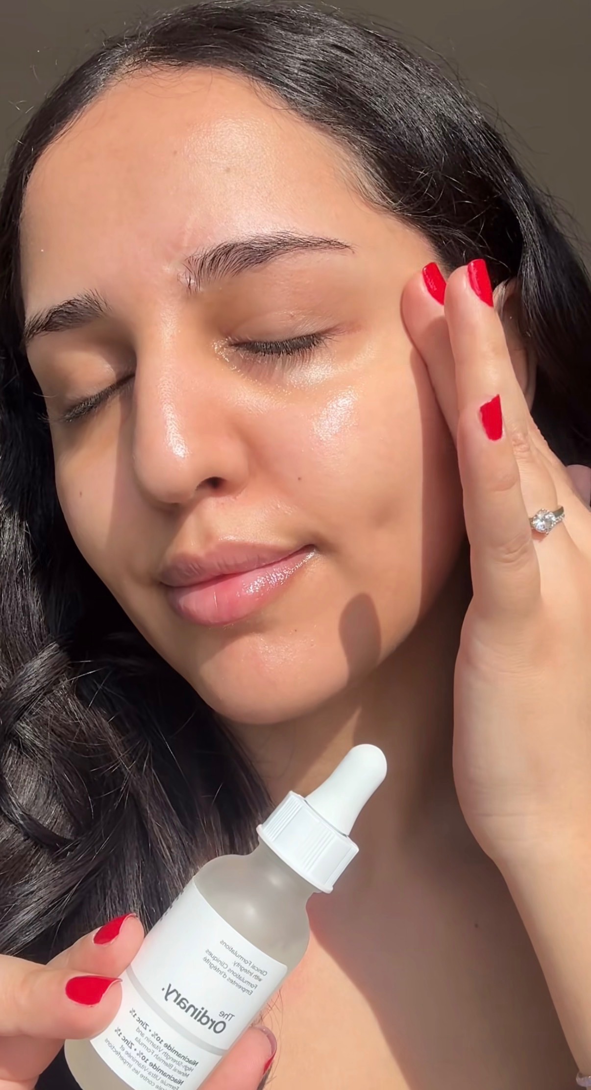 A person applying a skincare serum to their face, showcasing a natural glow and healthy skin.