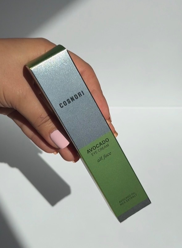 A hand holding a green and silver box of avocado eye cream from the brand Cosmodri.