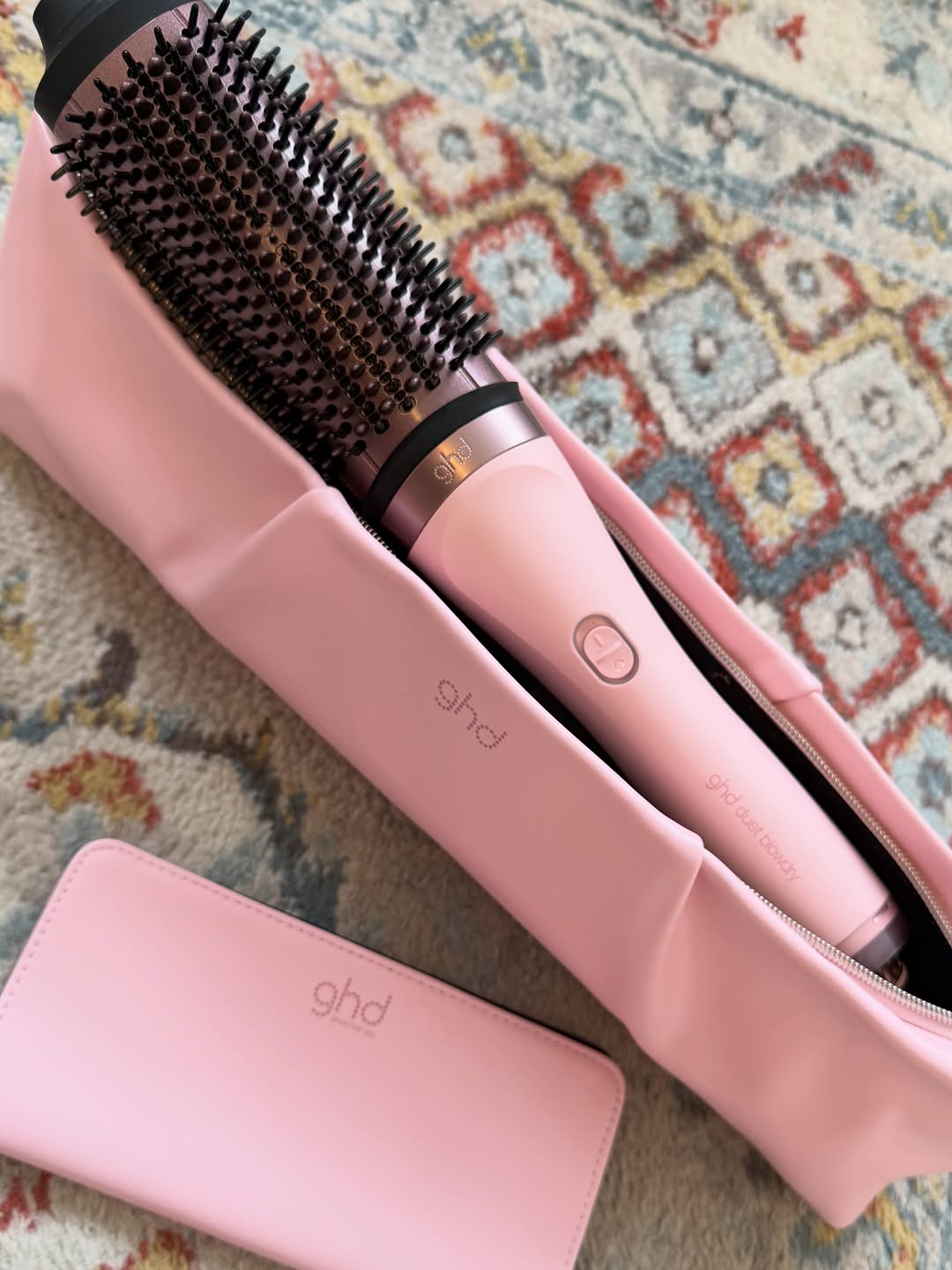 A pink hair styling tool and a matching case, both branded with 'ghd', are displayed on a patterned rug.