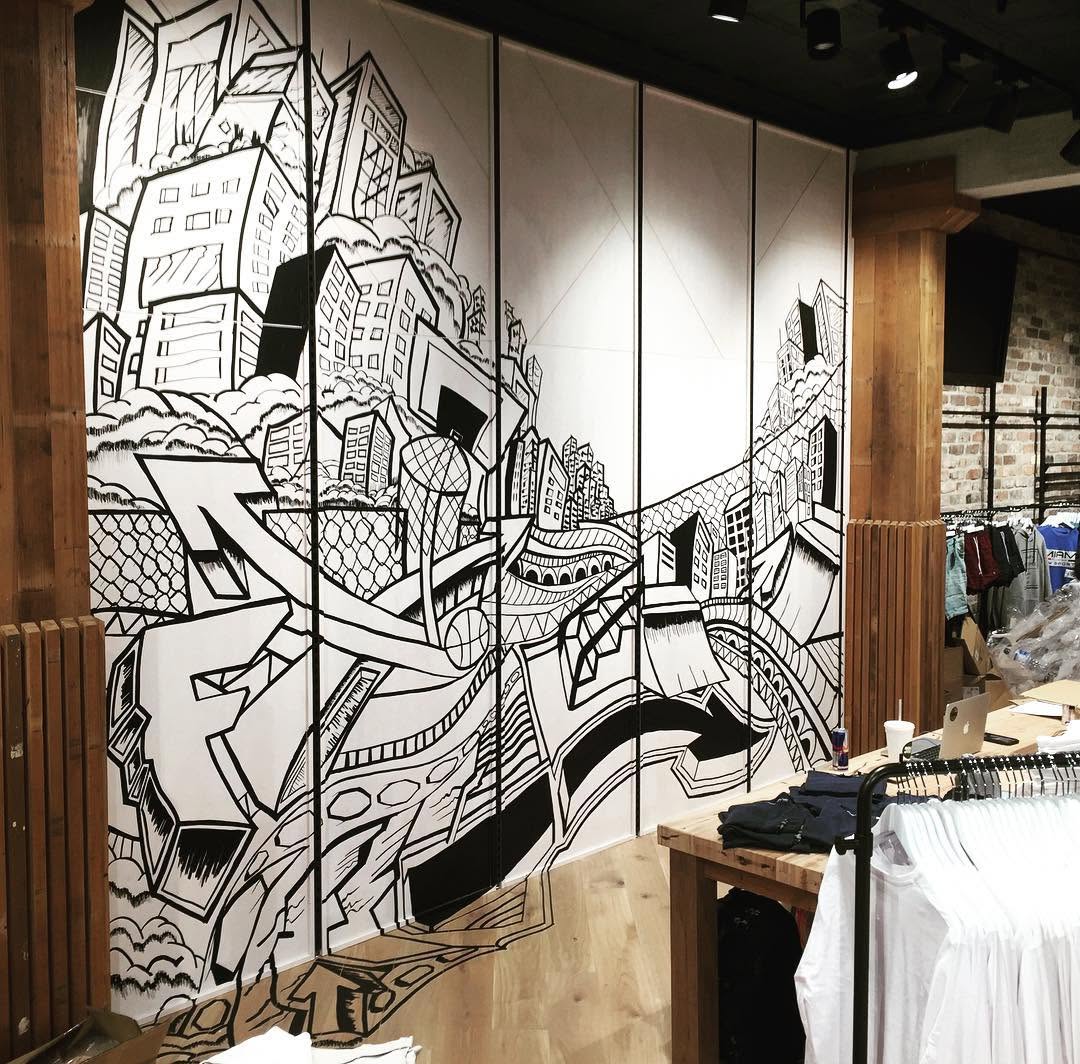 A large black and white mural depicting urban landscapes and abstract designs on a wall in a retail space.