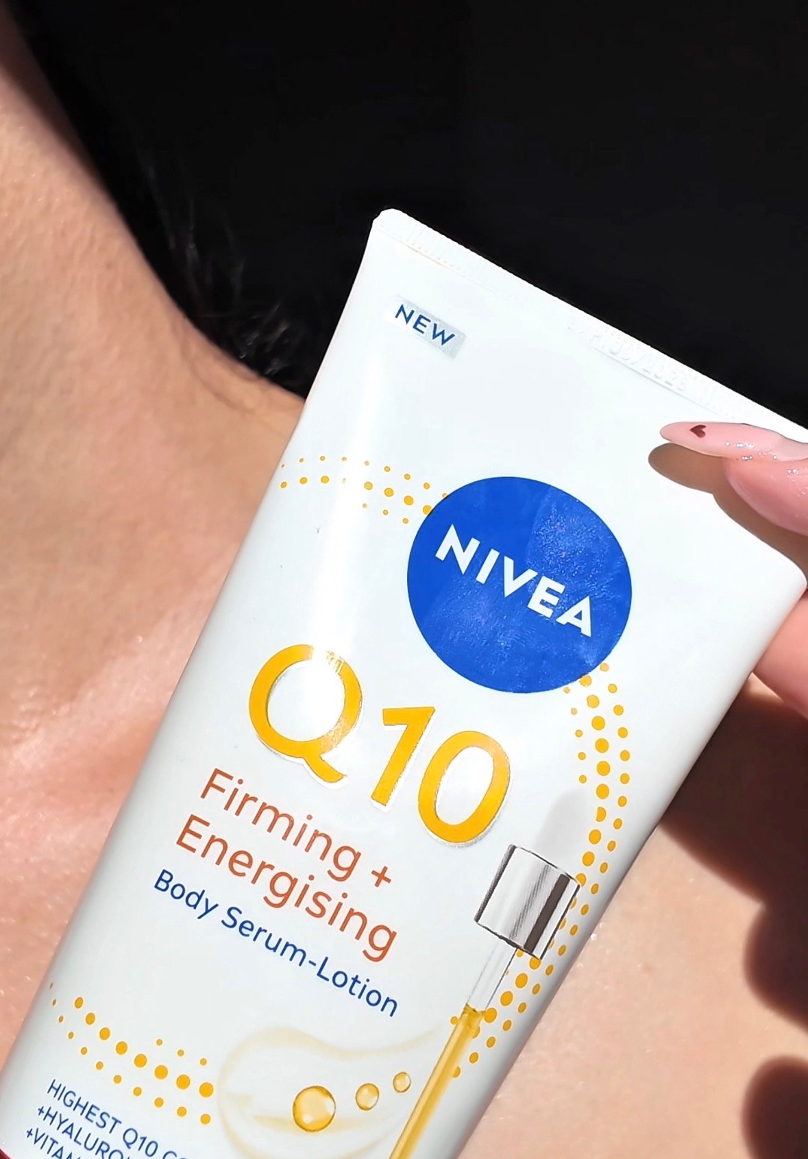 A close-up of a hand holding a NIVEA Q10 Firming + Energising Body Serum-Lotion tube against a blurred background.