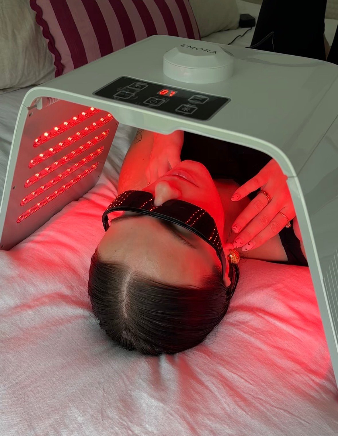 A person lying on a bed under a red light therapy device, wearing protective goggles and appearing relaxed.