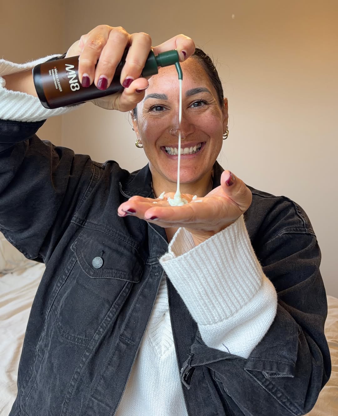 A person smiling while pouring a skincare product into their hand, showcasing the texture of the product.