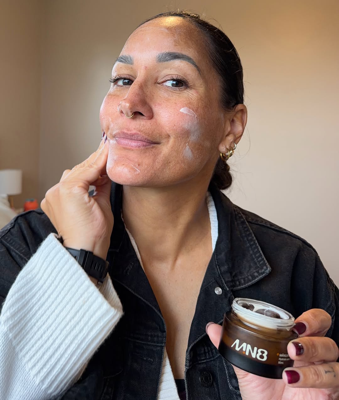 A woman applying a skincare product to her face while smiling, showcasing a natural beauty routine.