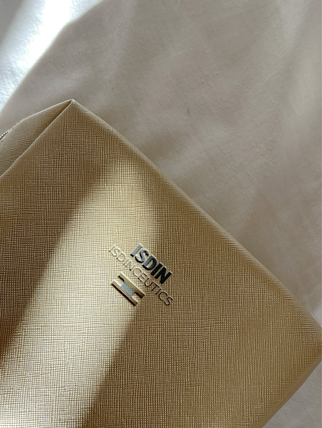 A close-up of a gold-colored packaging with the brand name 'ISDIN' prominently displayed.