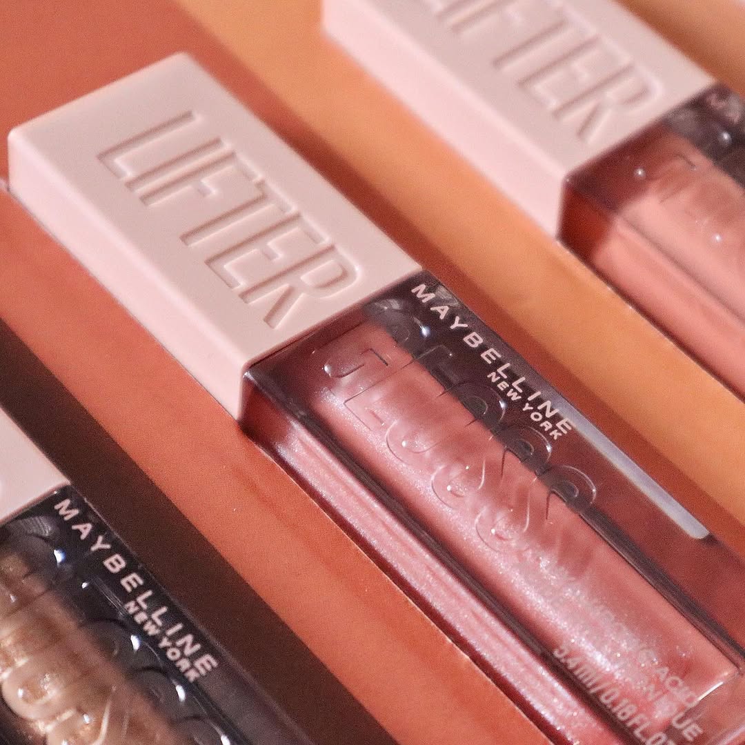 A close-up of Maybelline Lifter Gloss lip products arranged on a colorful background, showcasing various shades.