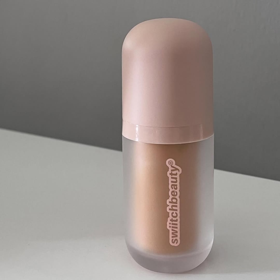 A sleek, modern beauty product in a frosted bottle with a pink cap, placed on a white surface against a gray background.