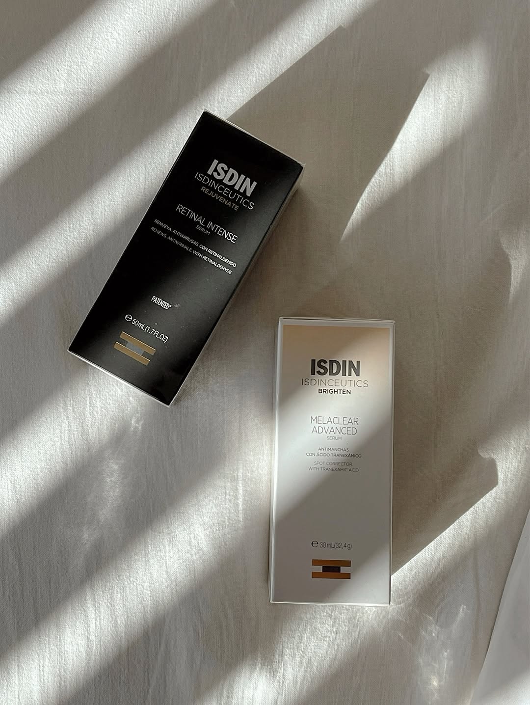 Two skincare product boxes placed on a soft, light-colored fabric surface, showcasing their elegant packaging design.