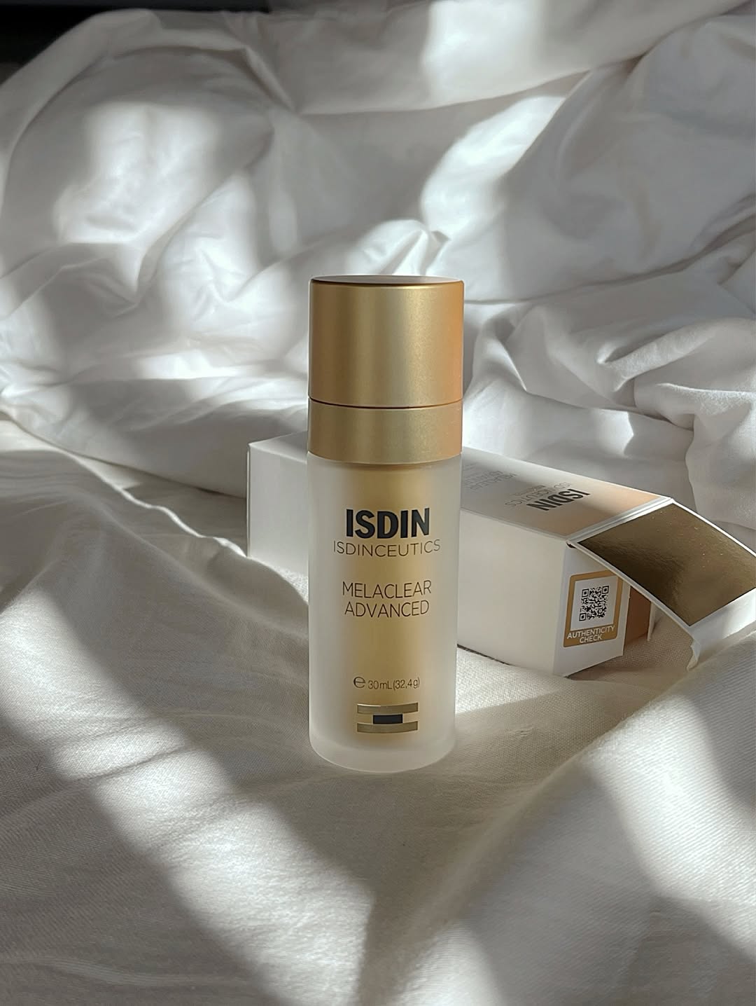 A bottle of ISDIN Melaclear Advanced skincare product placed on a soft, white fabric surface, with soft shadows creating a serene atmosphere.
