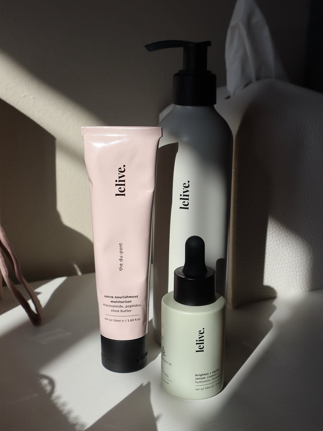 A collection of skincare products displayed on a surface, featuring a pink tube, a gray bottle, and a green dropper bottle.
