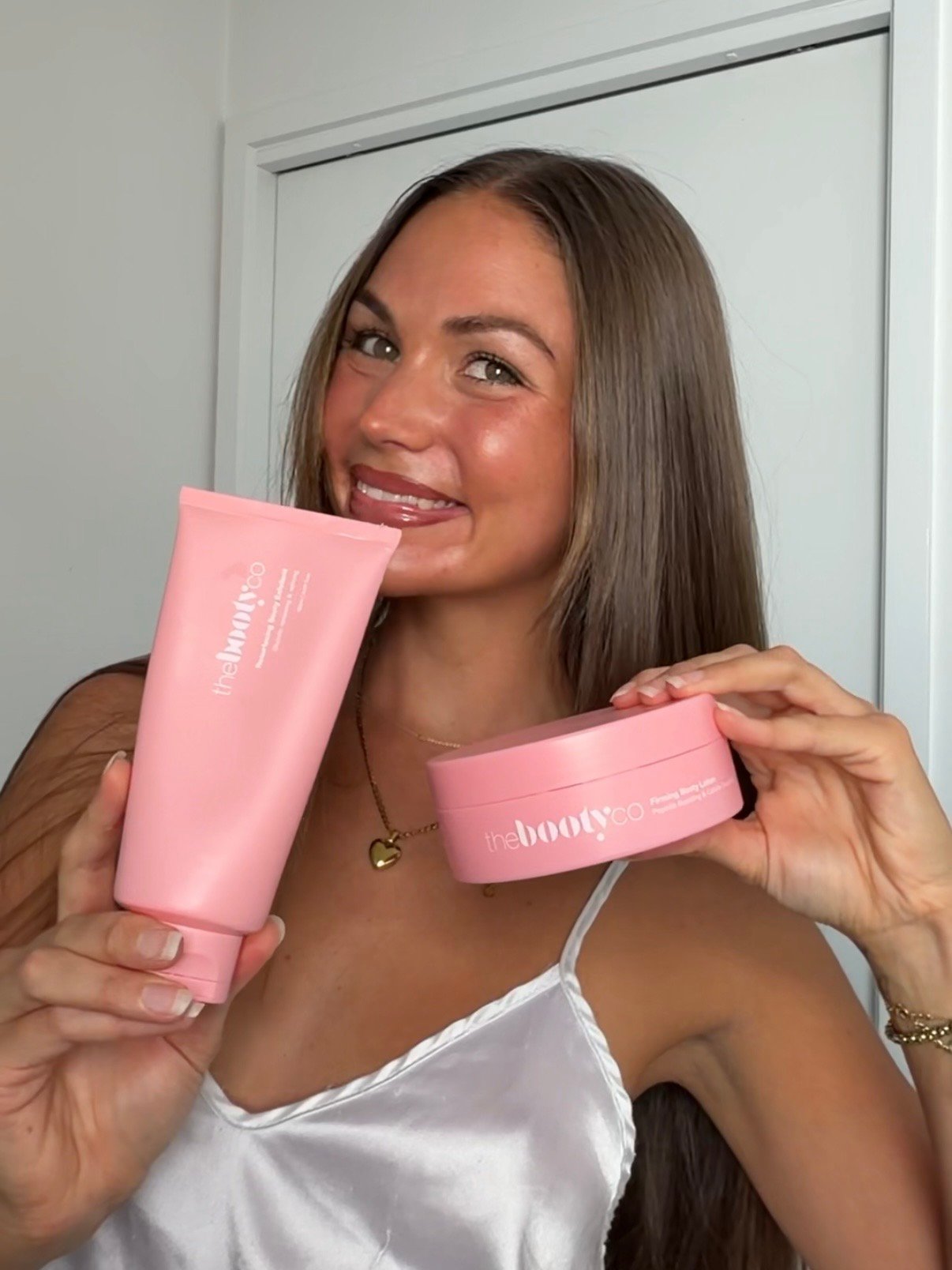 A person holding two pink skincare products, smiling and showcasing the items in a bright setting.