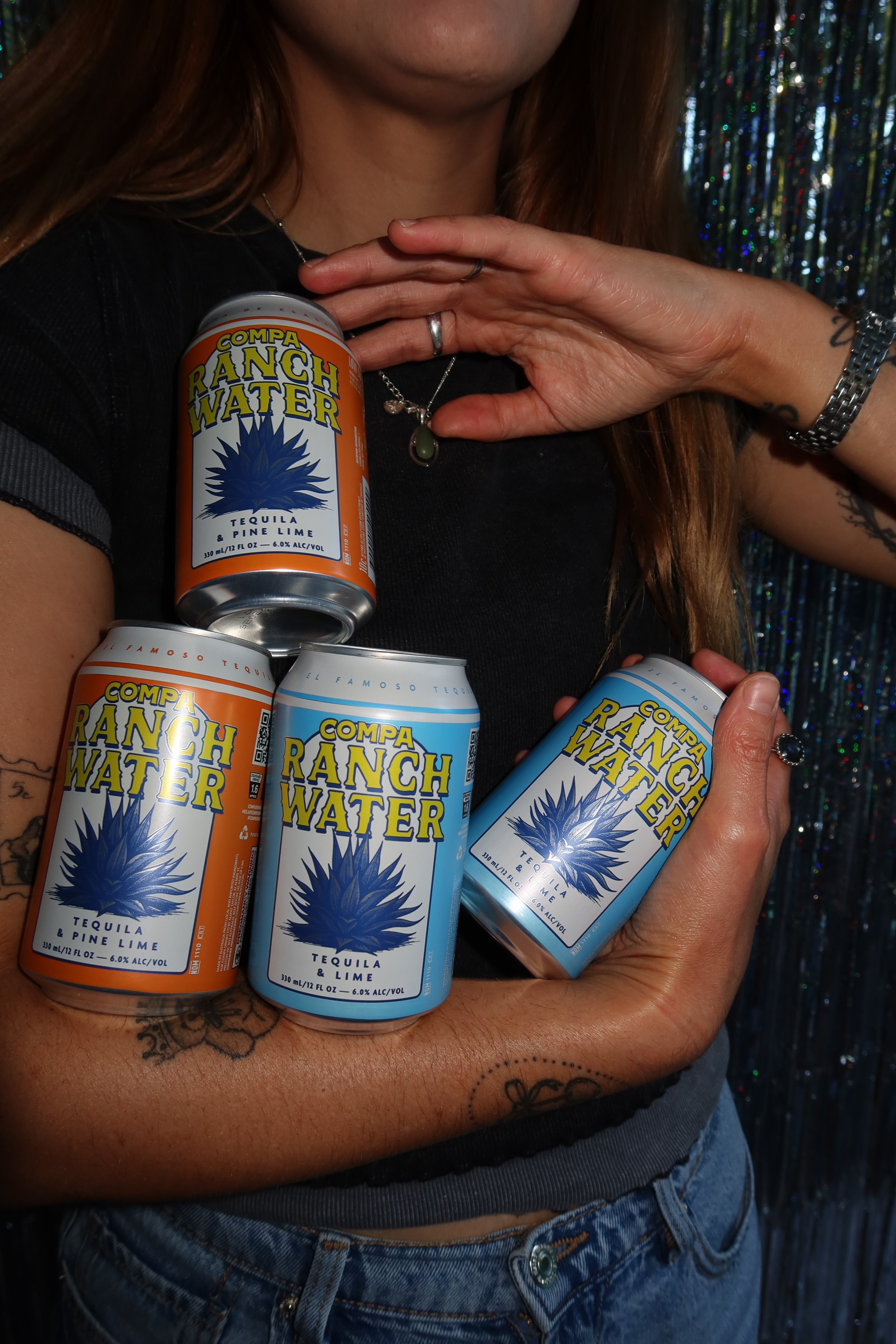 A person holding four cans of Ranch Water, showcasing the vibrant designs against a shimmering backdrop.