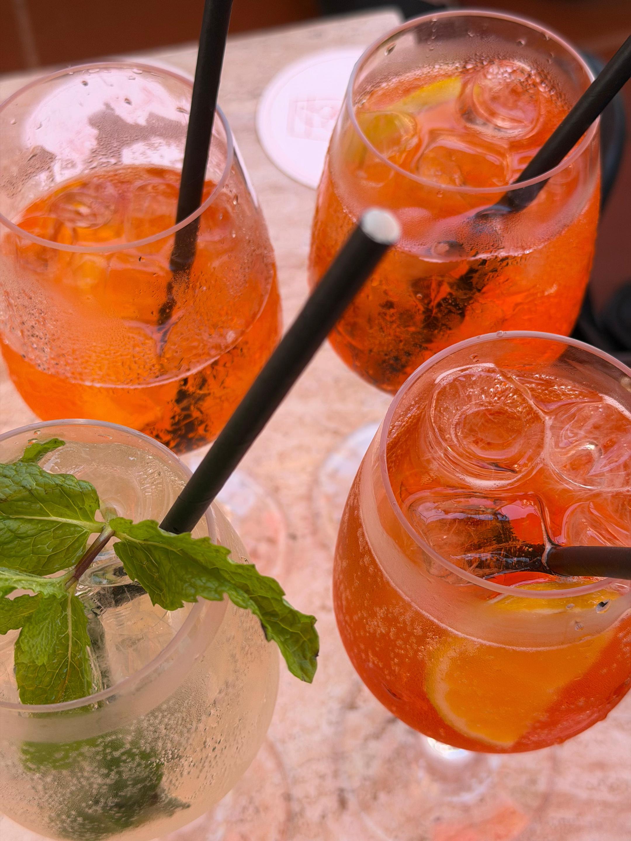 A close-up view of four colorful cocktails, featuring mint and lemon garnishes, served in clear glasses with straws.