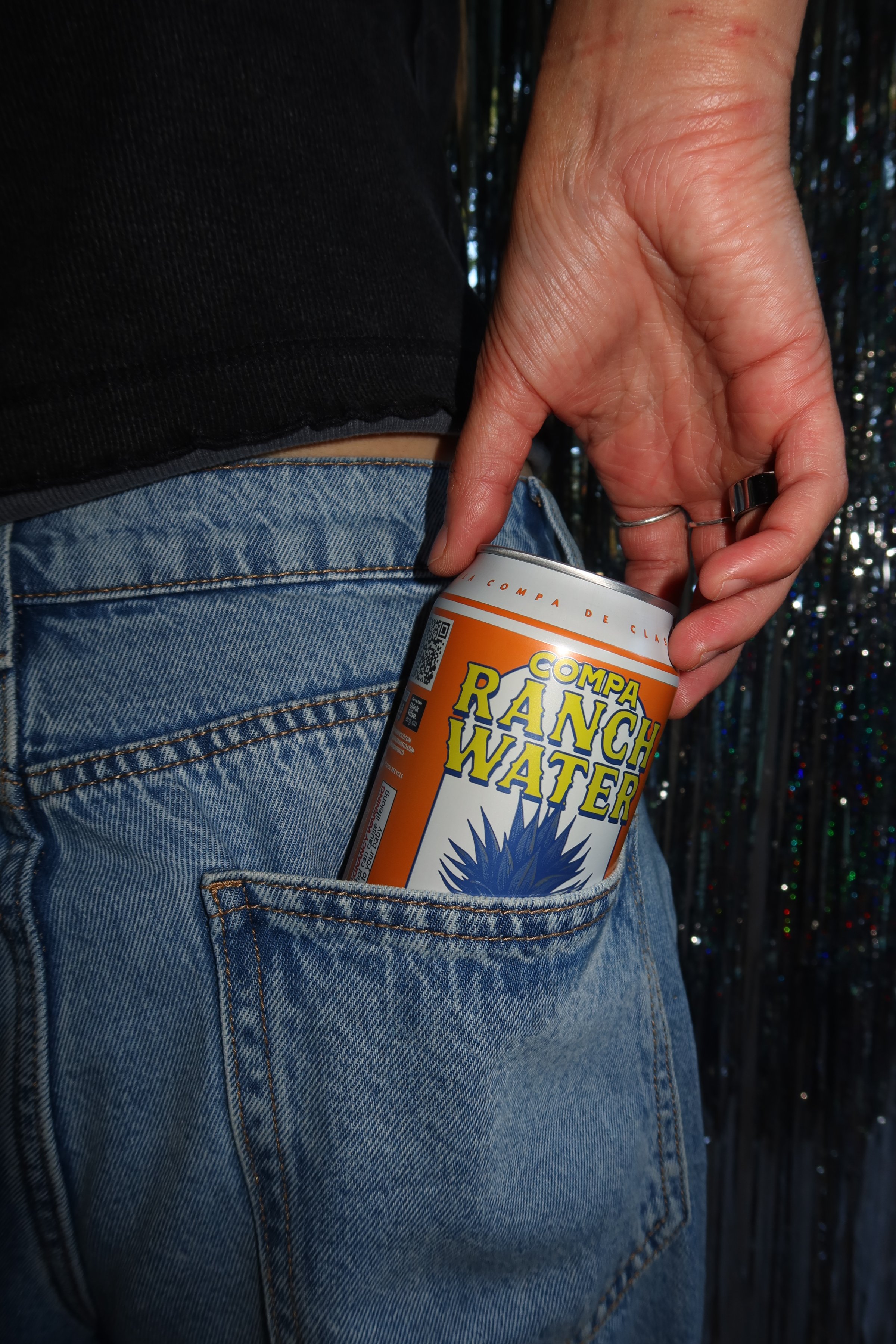 A hand holding a can of Ranch Water is partially visible as it is tucked into the back pocket of a pair of blue jeans.