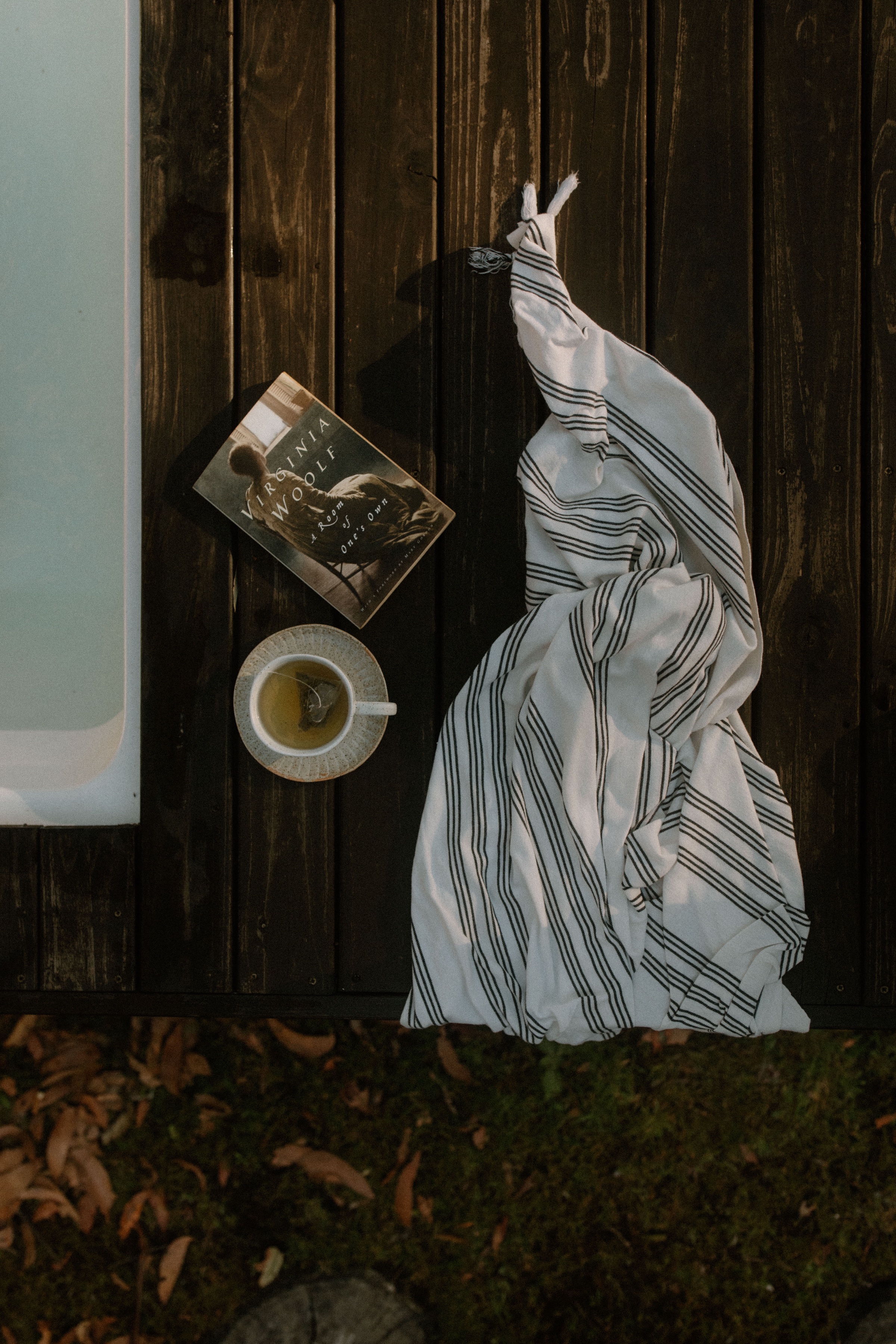 A striped white blanket draped over a wooden surface next to a book and a cup of tea.