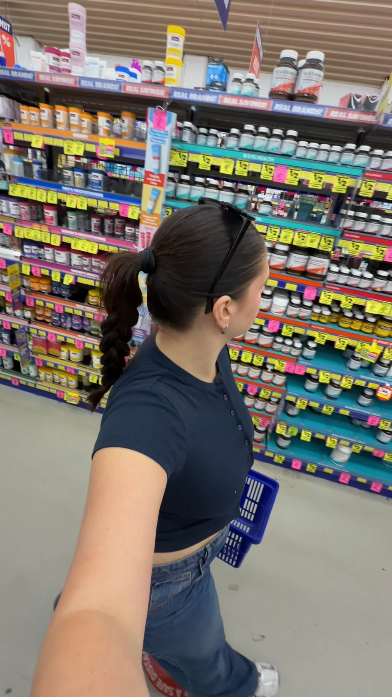 A person with long hair in a ponytail stands in an aisle of a store, surrounded by colorful shelves filled with various products.