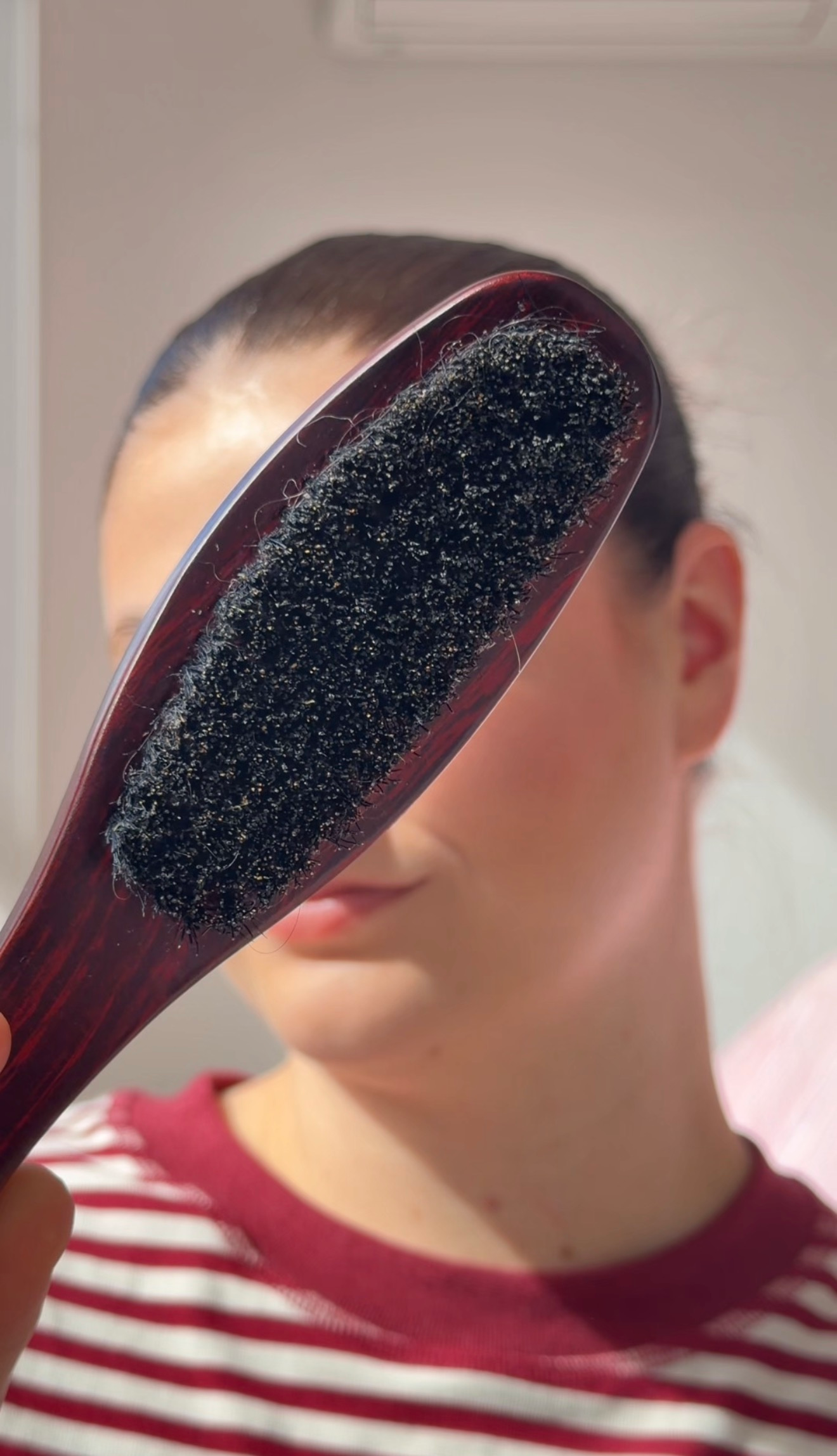 A close-up of a hairbrush held in front of a person's face, showcasing the bristles covered in hair.