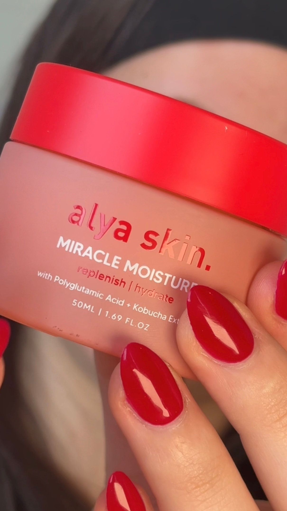 A close-up of a hand holding a jar of Alya Skin Miracle Moisturizer, showcasing its red lid and label.