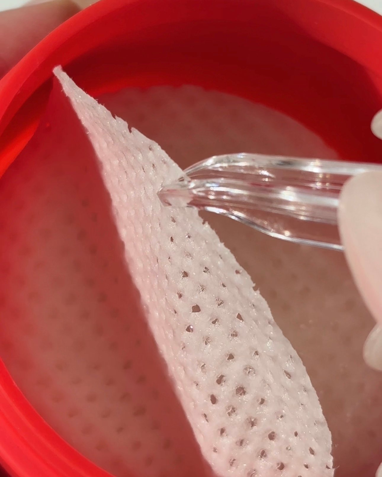 A close-up view of a red container with a textured, pink material being handled with a dropper.