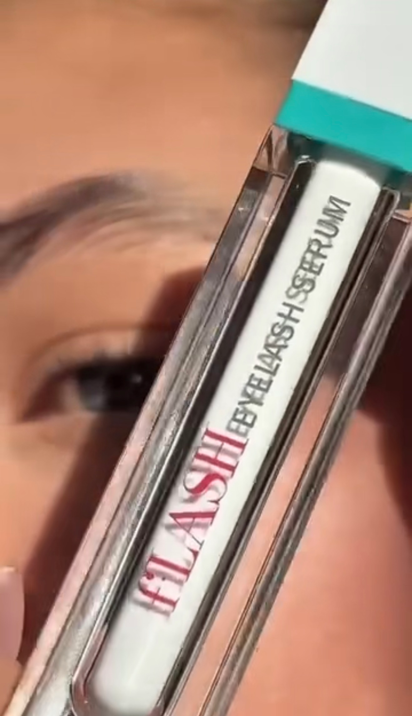 Close-up of a person's eye with a focus on a tube of eyelash serum labeled 'FLASH'.