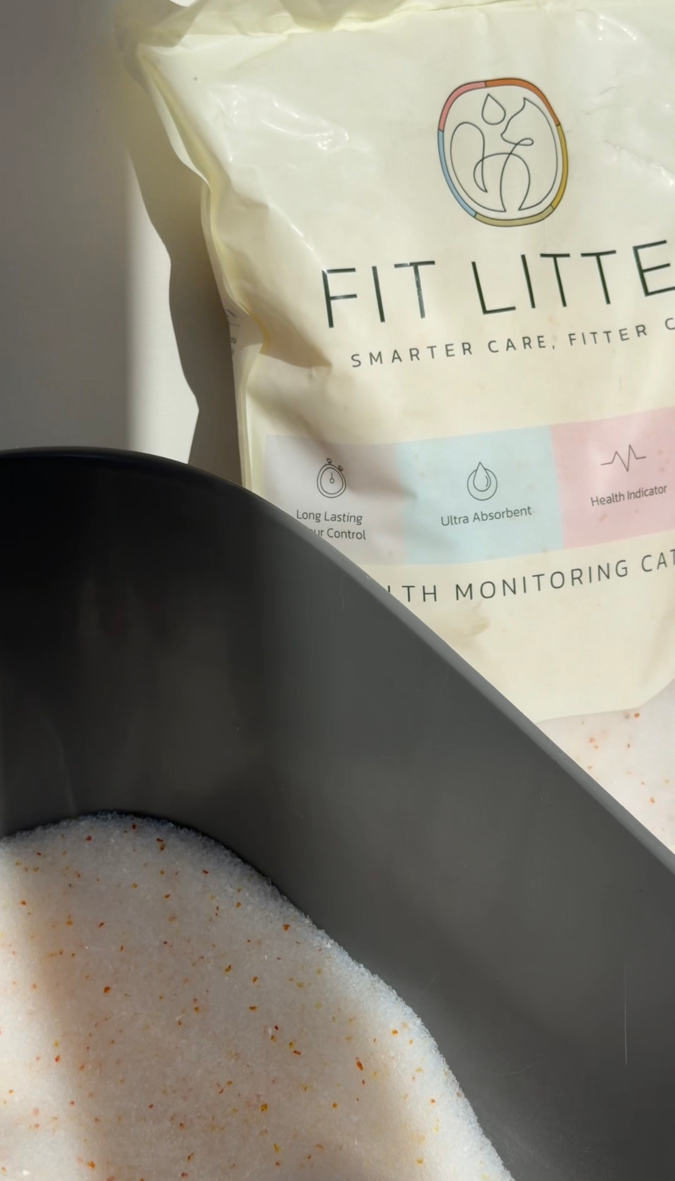 A close-up of cat litter in a gray litter box with a bag of Fit Litter in the background, showcasing its features.