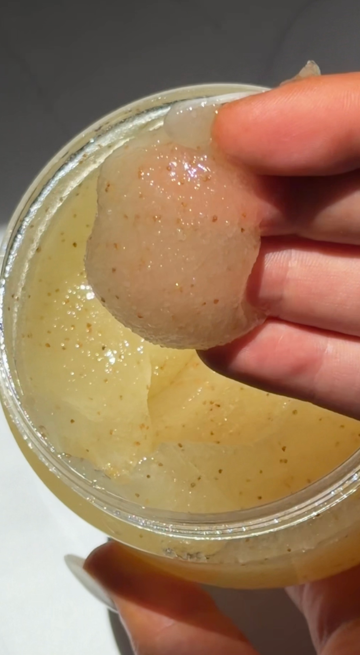 A close-up of a hand holding a translucent, gel-like substance from a jar, showcasing its texture and shimmer.