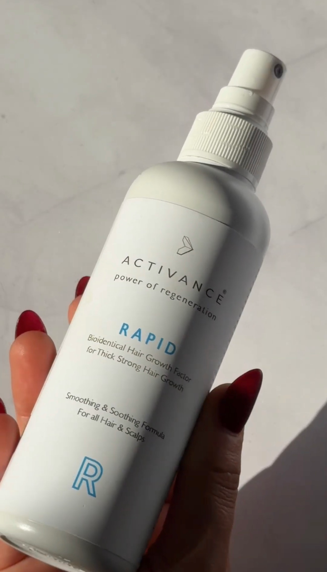 A hand holding a bottle of Activance Rapid, a hair growth spray, against a light background.