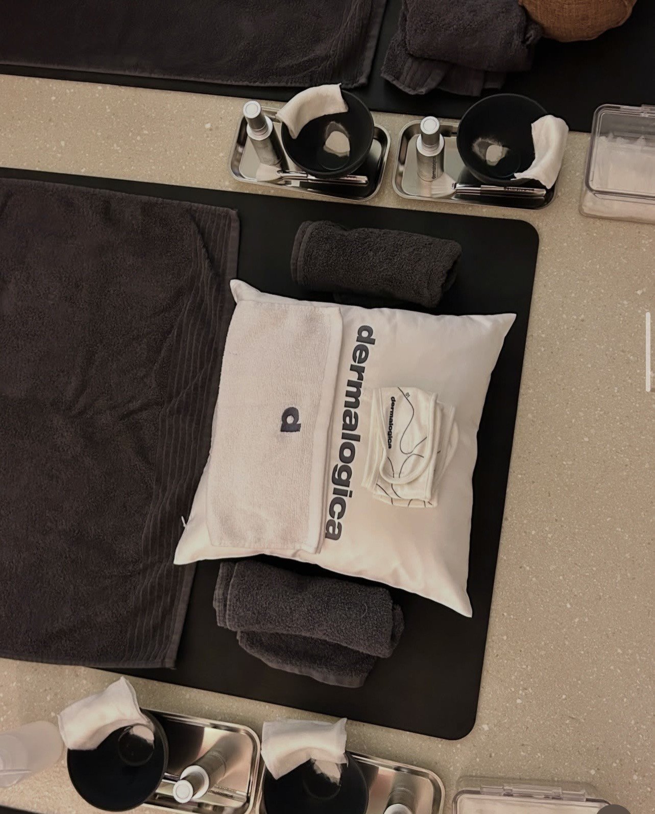 A neatly arranged spa setup featuring a Dermalogica branded pillow, towels, and various skincare products on a countertop.
