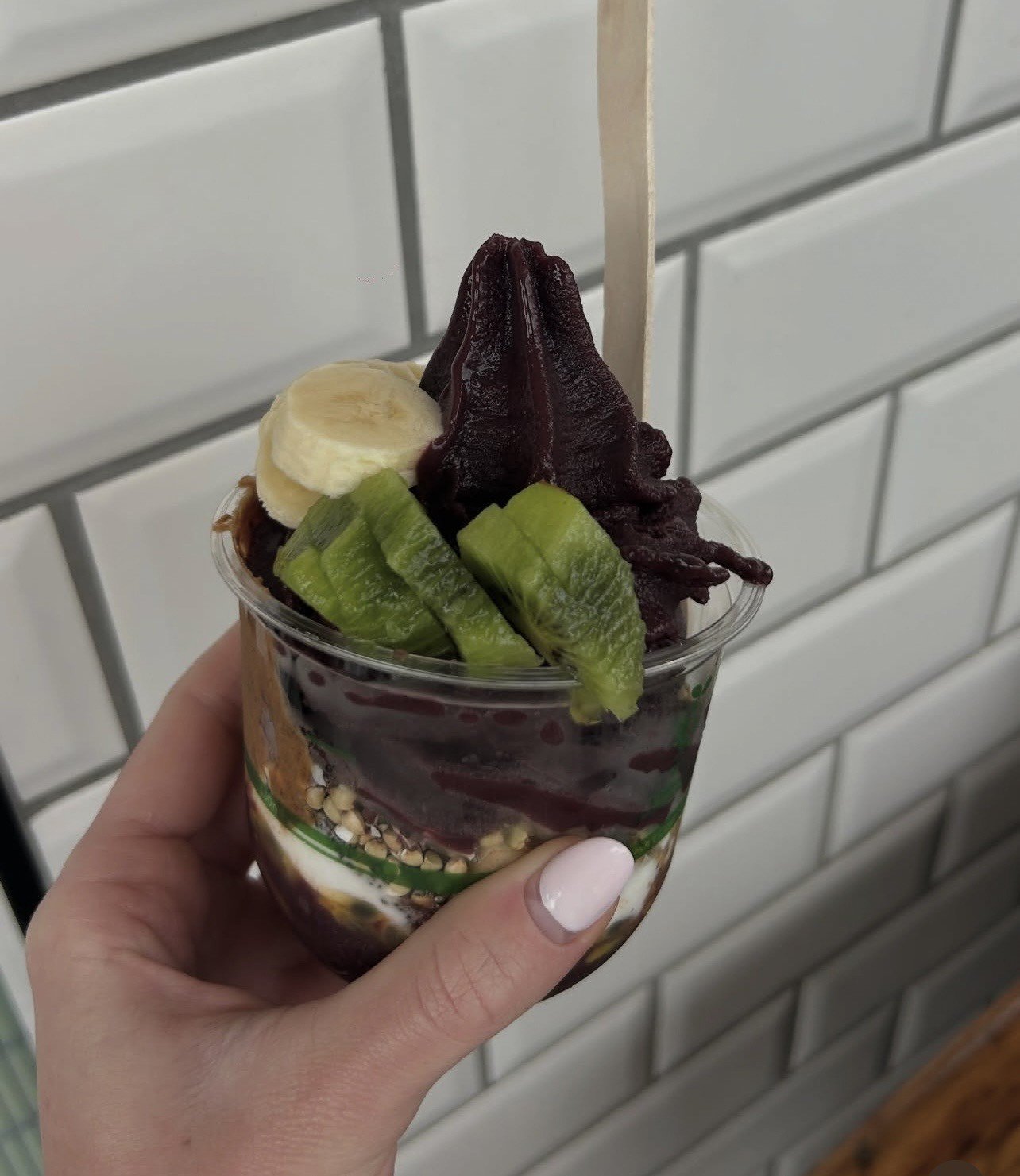 A hand holding a cup of acai bowl topped with banana slices and kiwi.