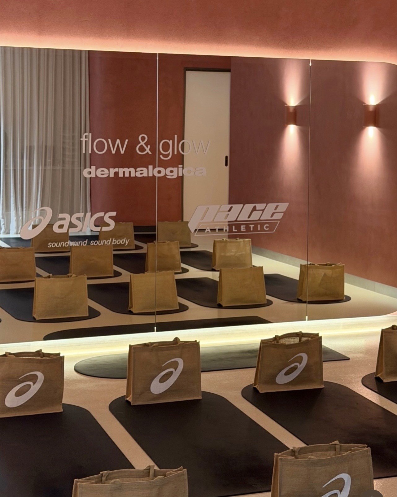 A serene yoga studio with mats arranged neatly on the floor, featuring branded bags for participants. The warm-toned walls and soft lighting create a calming atmosphere.