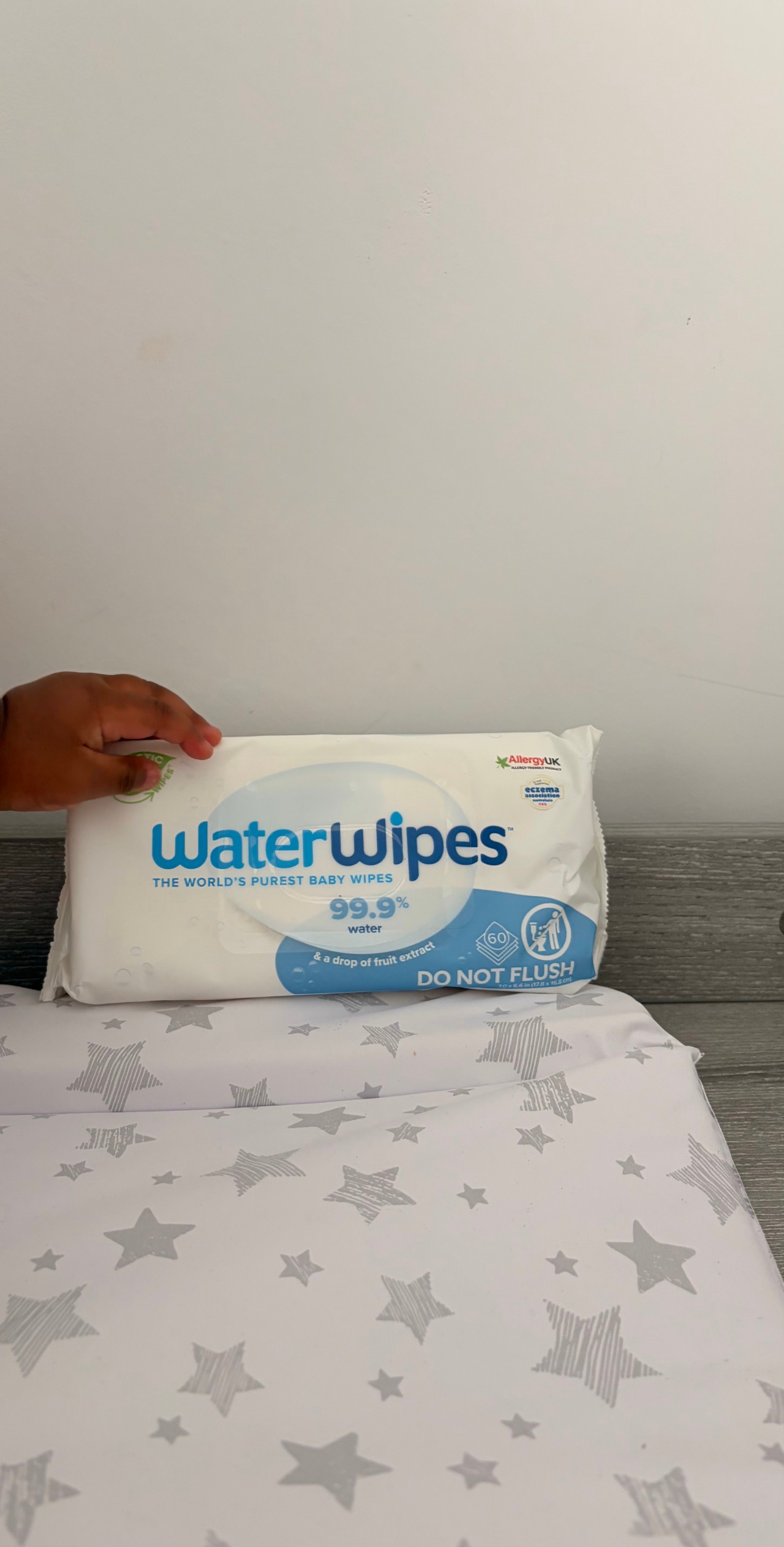 A child's hand holding a pack of WaterWipes, the world's purest baby wipes, placed on a star-patterned surface.
