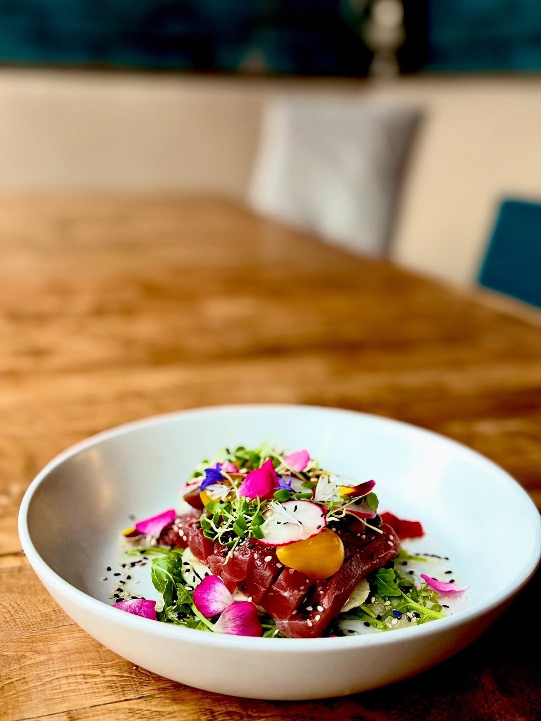A beautifully plated dish featuring raw tuna on a bed of greens, garnished with colorful edible flowers and herbs.