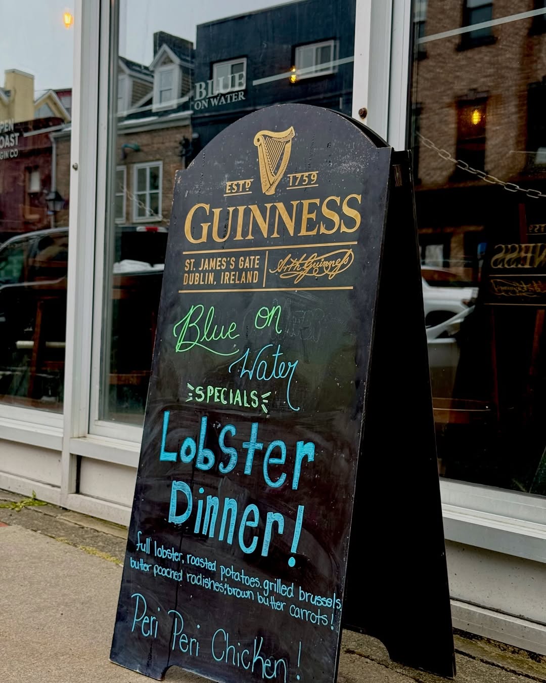 A chalkboard sign advertising a lobster dinner special outside a restaurant, featuring the Guinness logo and colorful handwritten text.