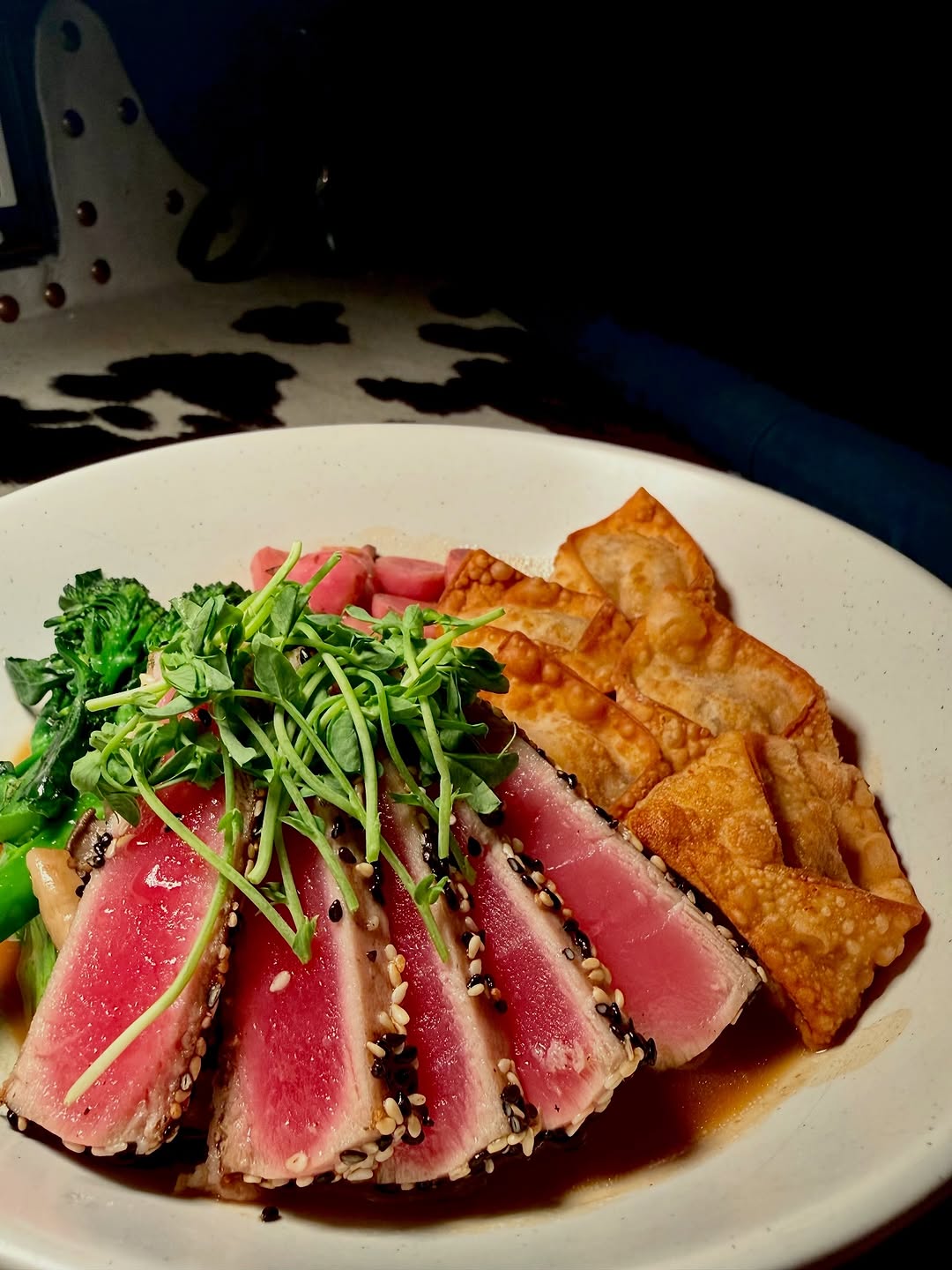 A beautifully arranged plate featuring sliced seared tuna topped with sesame seeds, accompanied by crispy wontons and garnished with microgreens and pickled vegetables.