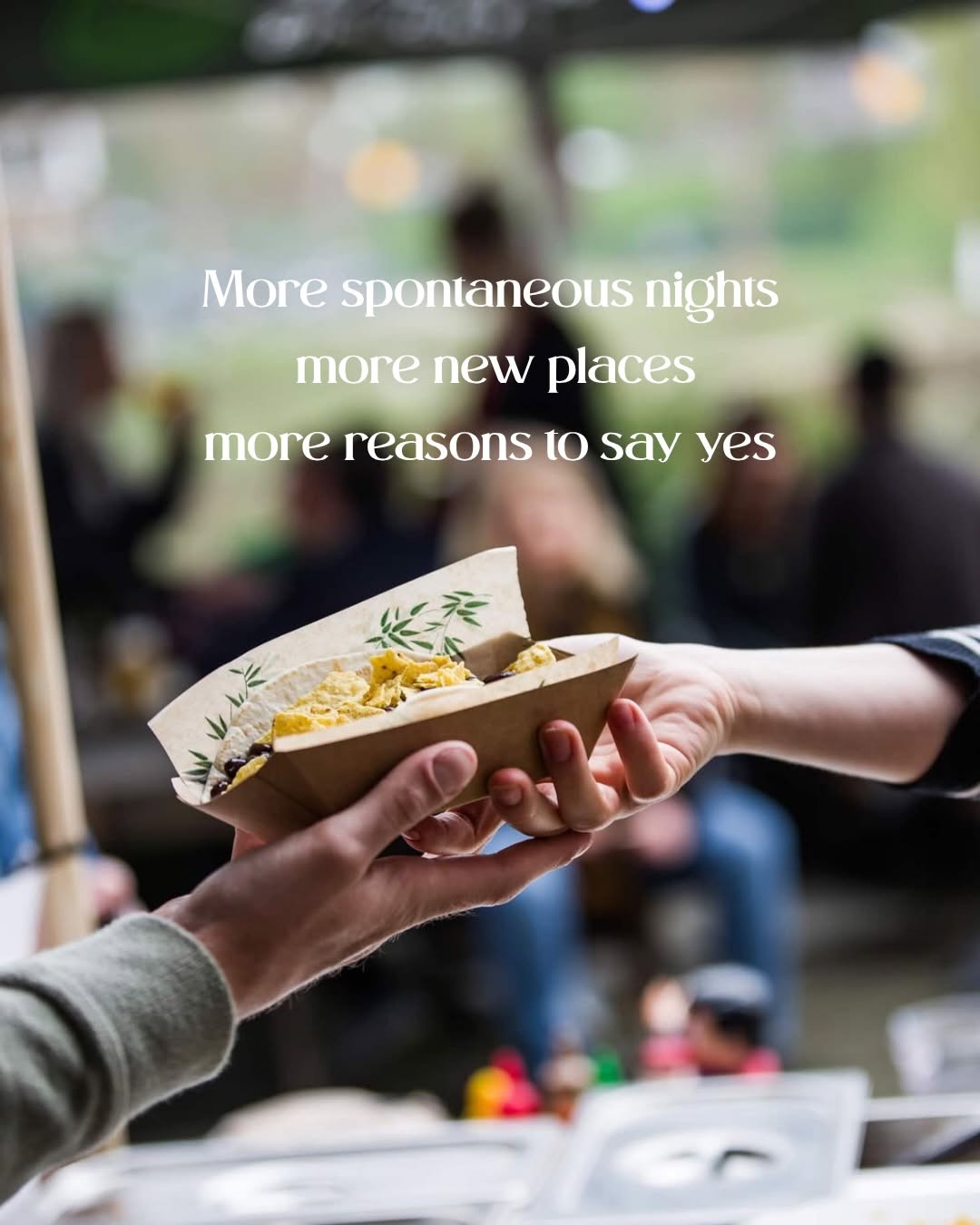 A hand is reaching out to receive a food container, suggesting a moment of sharing and enjoyment in a lively outdoor setting.