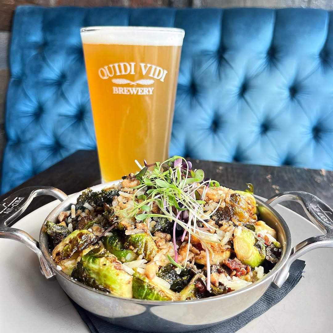 A vibrant dish featuring Brussels sprouts, rice, and garnished with microgreens, served on a plate next to a glass of beer from Quidi Vidi Brewery.