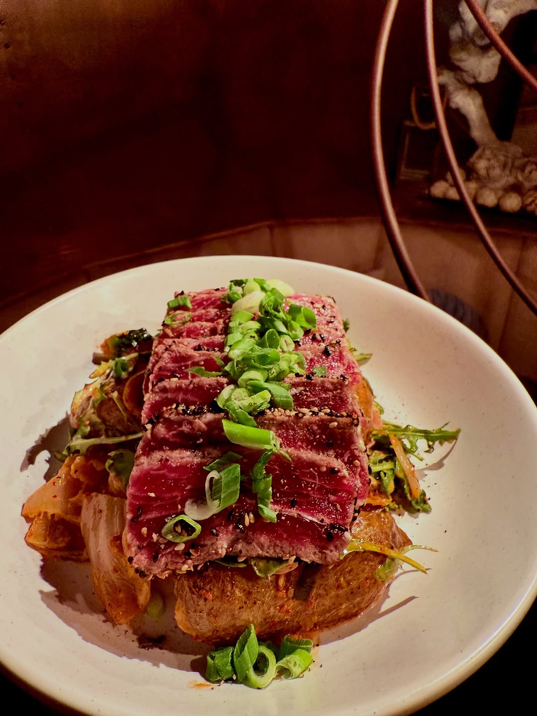 A beautifully plated dish featuring slices of beef on a bed of kimchi and vegetables, garnished with green onions.