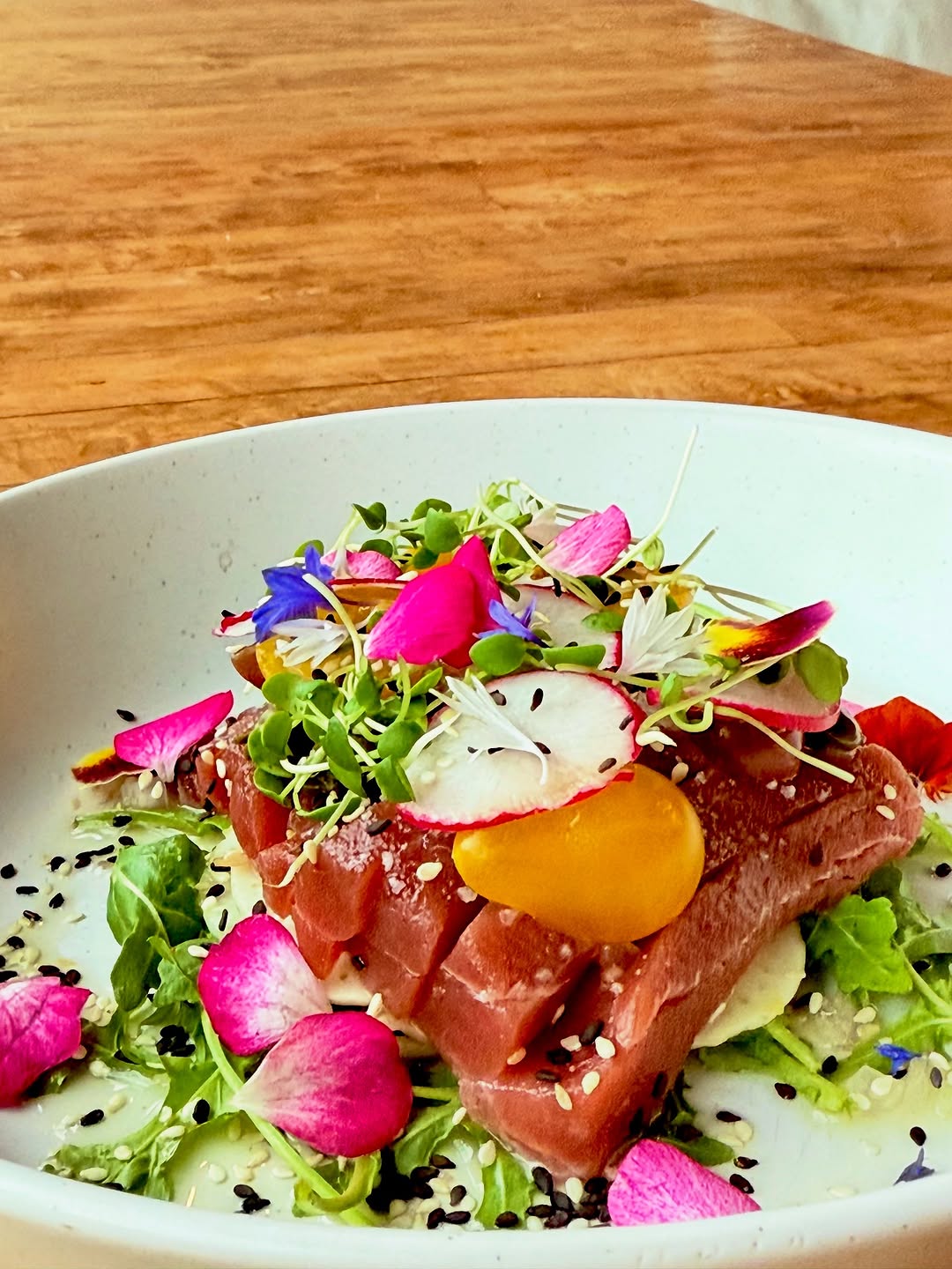 A beautifully plated dish featuring fresh tuna, garnished with colorful edible flowers and microgreens on a bed of greens.