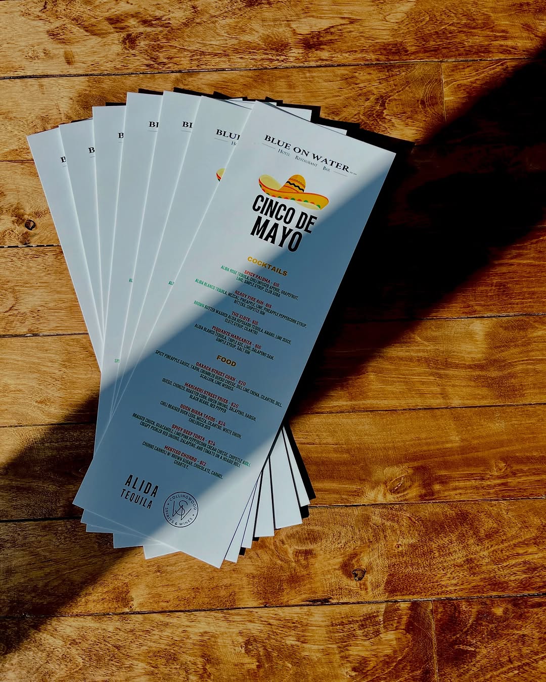 A collection of menus for a Cinco de Mayo event laid out on a wooden surface, with shadows creating a dynamic pattern.