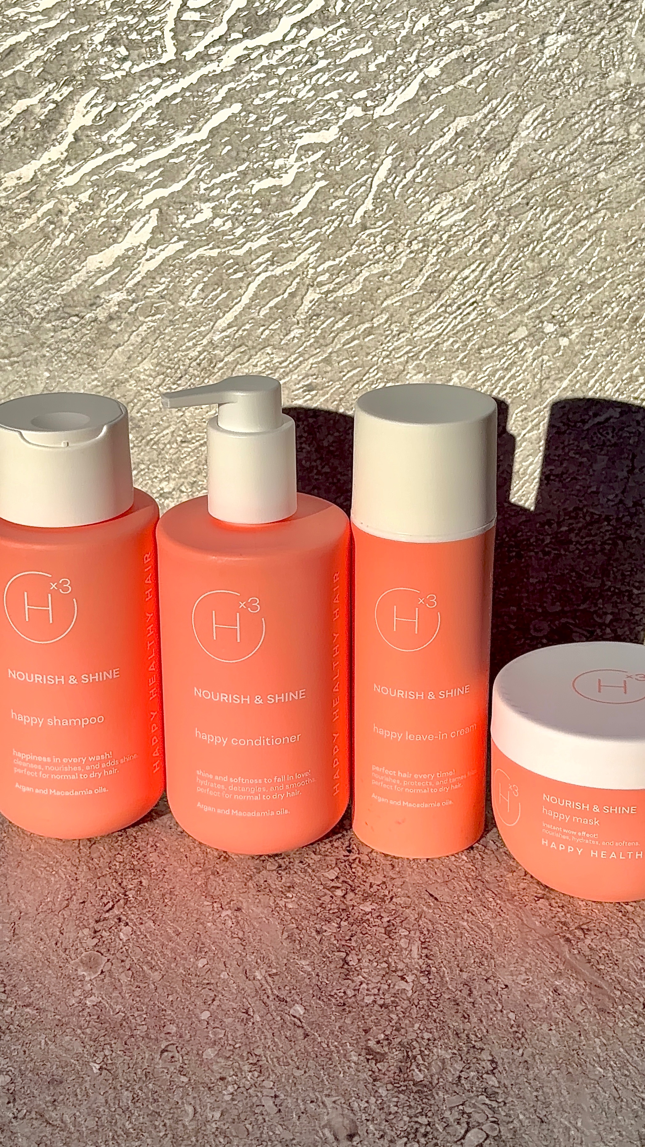 A collection of hair care products displayed against a textured background, featuring shampoo, conditioner, and a hair mask in vibrant orange packaging.